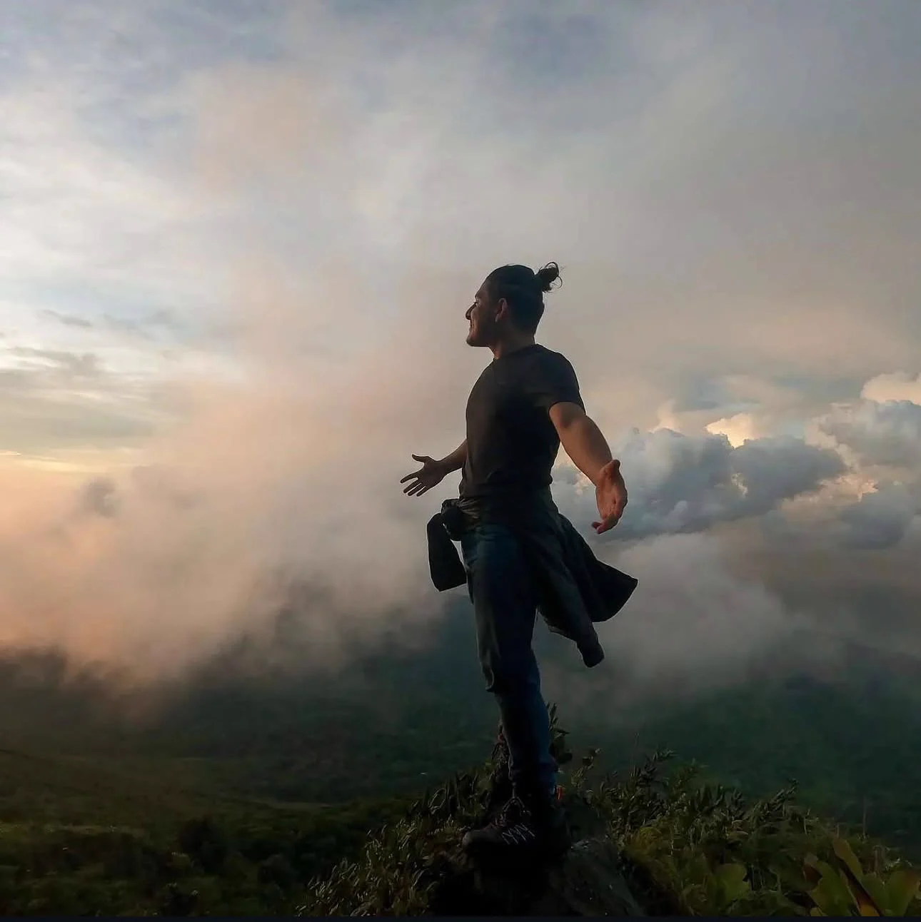 Benjamín Bautista standing on a mountain summit above the clouds, arms open